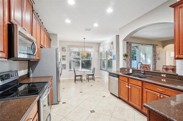 kitchen featuring dark stone counters, stainless steel appliances, sink, light tile patterned floors, and hanging light fixtures