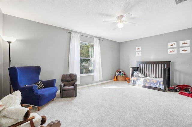 carpeted bedroom with ceiling fan, a nursery area, and a textured ceiling