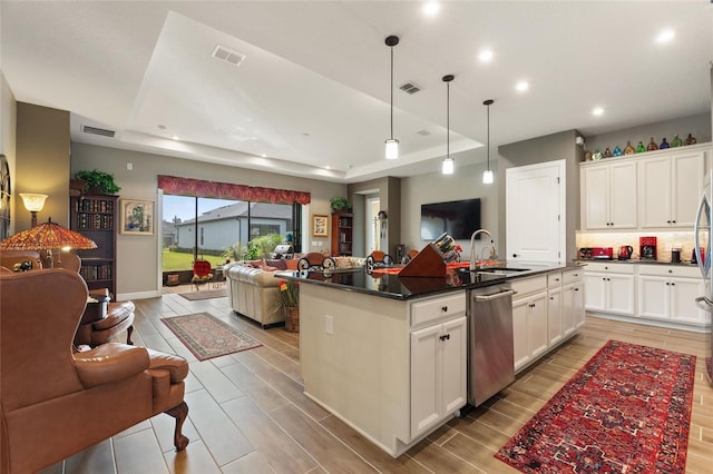 kitchen with dishwasher, a raised ceiling, light wood-type flooring, and a kitchen island with sink