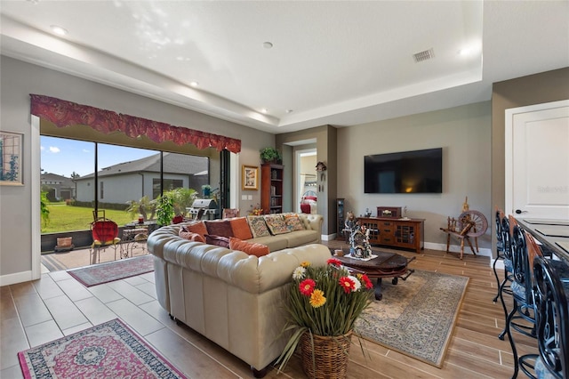 living room with light hardwood / wood-style floors and a raised ceiling