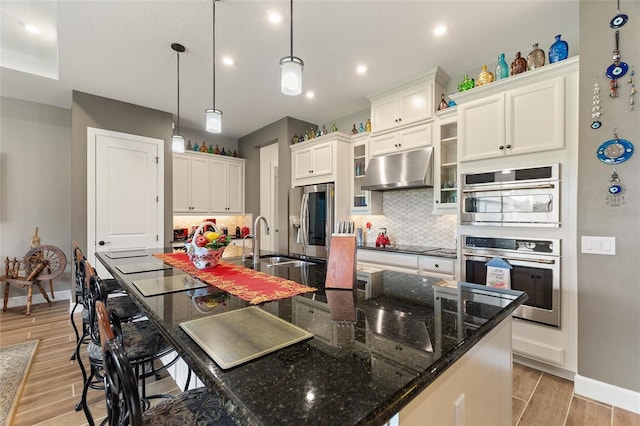 kitchen with decorative backsplash, light wood-type flooring, stainless steel appliances, a spacious island, and decorative light fixtures