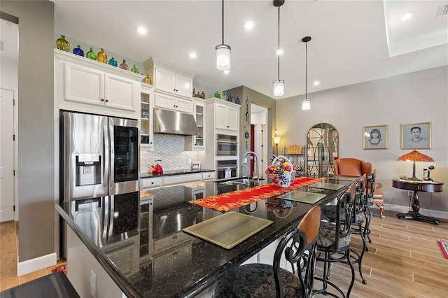 kitchen with white cabinetry, light hardwood / wood-style flooring, a large island with sink, pendant lighting, and appliances with stainless steel finishes