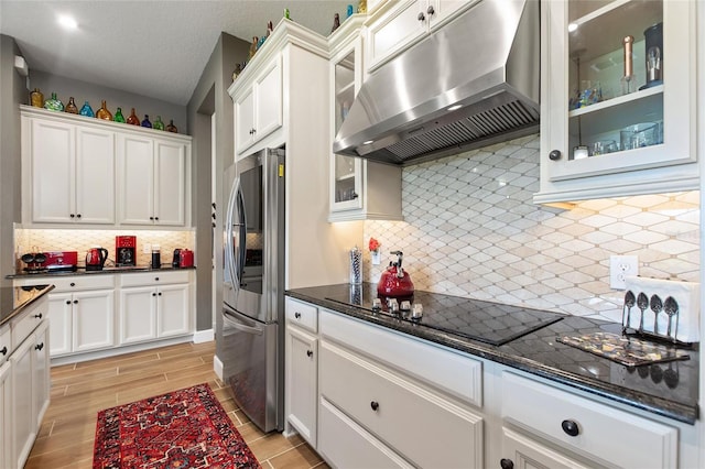 kitchen with stainless steel refrigerator with ice dispenser, light hardwood / wood-style floors, decorative backsplash, black stovetop, and white cabinets