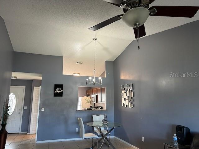 tiled dining area featuring a textured ceiling, ceiling fan with notable chandelier, and vaulted ceiling