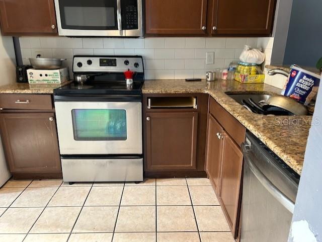 kitchen featuring decorative backsplash, stainless steel appliances, sink, light tile patterned floors, and stone countertops