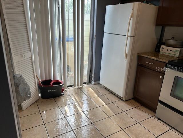 kitchen featuring stainless steel electric stove, white refrigerator, light tile patterned floors, and a wealth of natural light