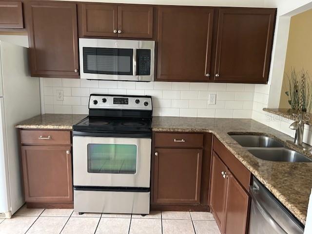 kitchen with a sink, appliances with stainless steel finishes, decorative backsplash, and dark stone countertops