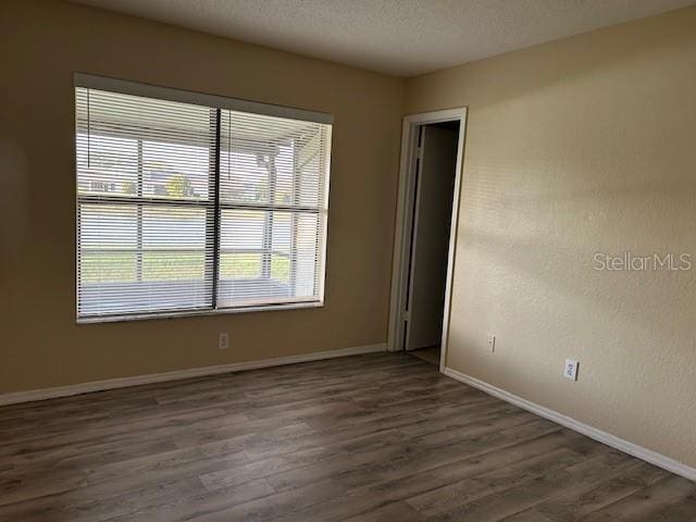 empty room with a textured ceiling, wood finished floors, and baseboards