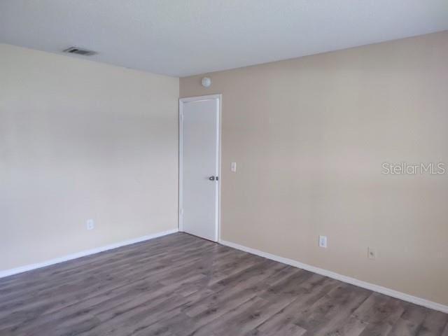 unfurnished room featuring baseboards, visible vents, and wood finished floors