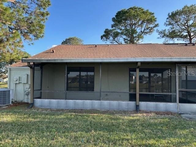 back of property with a shingled roof, cooling unit, a sunroom, and a lawn