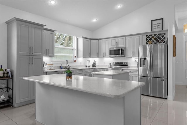 kitchen featuring appliances with stainless steel finishes, gray cabinetry, sink, a kitchen island, and lofted ceiling