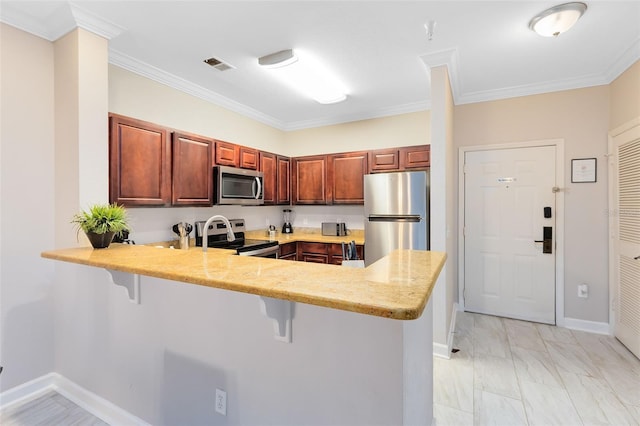 kitchen featuring a kitchen bar, stainless steel appliances, kitchen peninsula, and ornamental molding