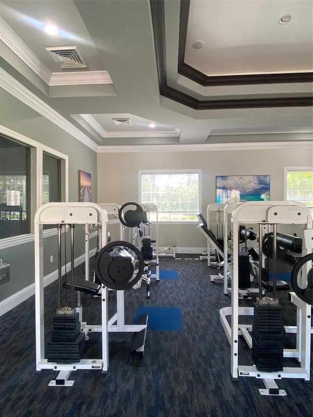 exercise room with a raised ceiling, dark carpet, and ornamental molding