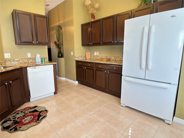 kitchen with light stone countertops, white appliances, light tile patterned floors, and dark brown cabinetry