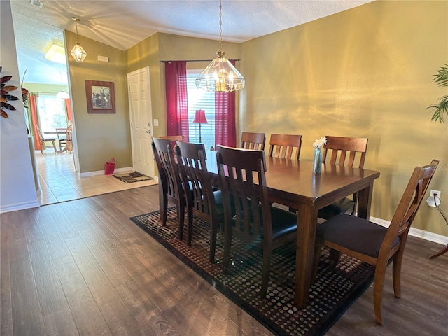 dining space featuring wood-type flooring, a textured ceiling, a notable chandelier, and vaulted ceiling