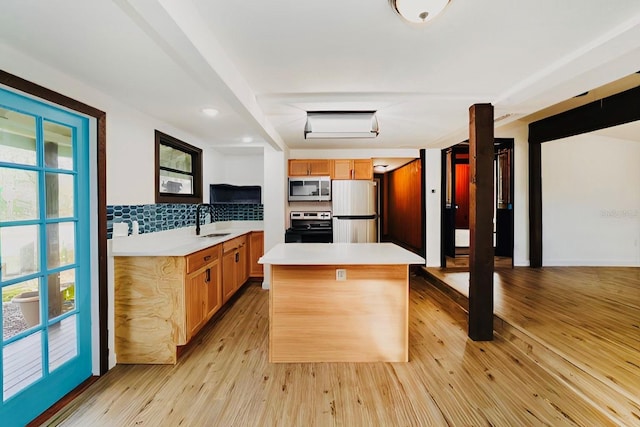 kitchen with light wood-style flooring, appliances with stainless steel finishes, a sink, light countertops, and backsplash