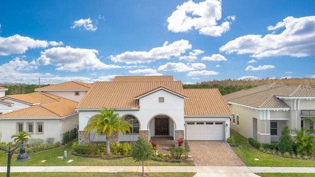 mediterranean / spanish home with a garage, a tiled roof, decorative driveway, a front lawn, and stucco siding