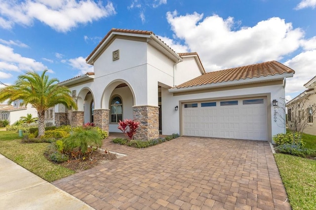 mediterranean / spanish-style home with an attached garage, a tile roof, decorative driveway, and stucco siding