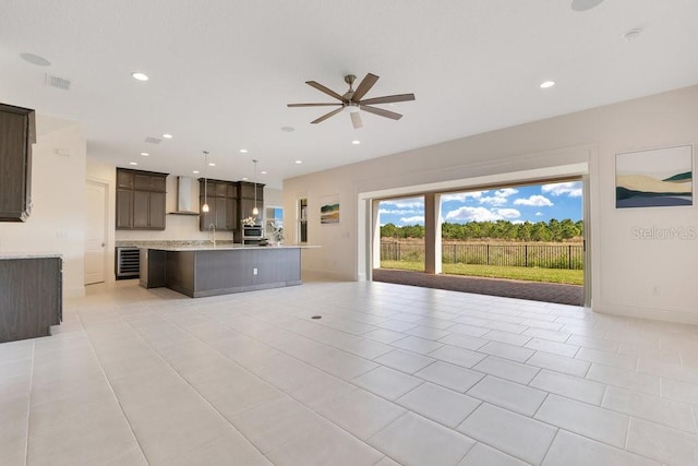 kitchen with light countertops, open floor plan, a kitchen island with sink, dark brown cabinetry, and wall chimney exhaust hood