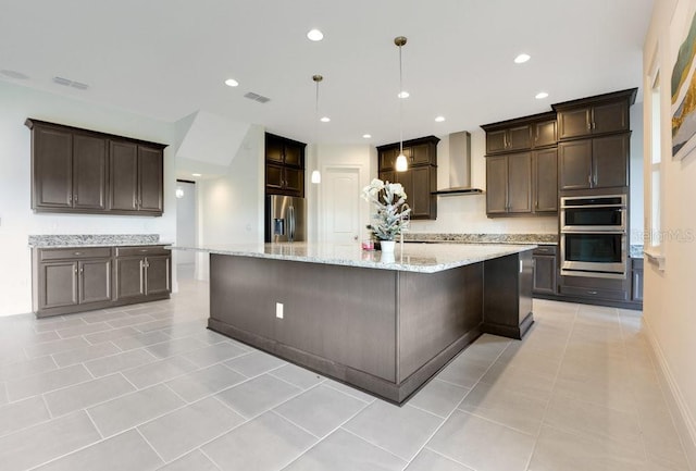 kitchen with dark brown cabinetry, wall chimney exhaust hood, a large island, stainless steel appliances, and pendant lighting