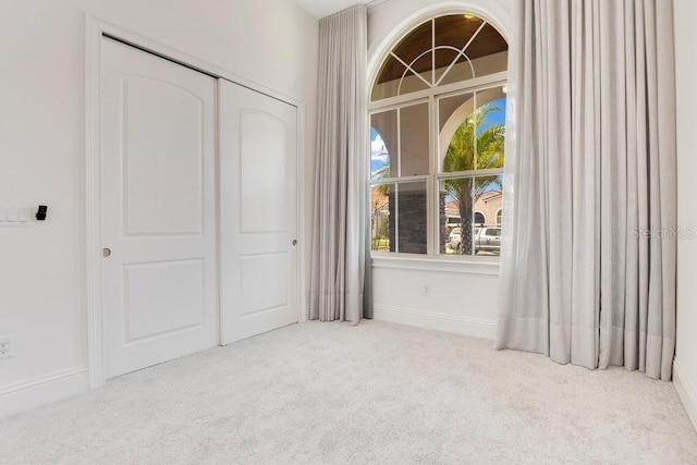 unfurnished bedroom with baseboards, a closet, and light colored carpet