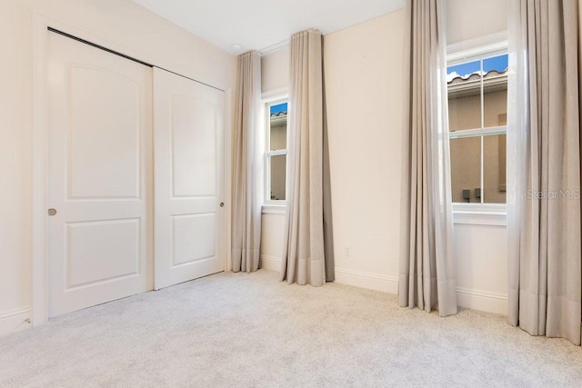 unfurnished bedroom featuring light carpet, baseboards, and a closet