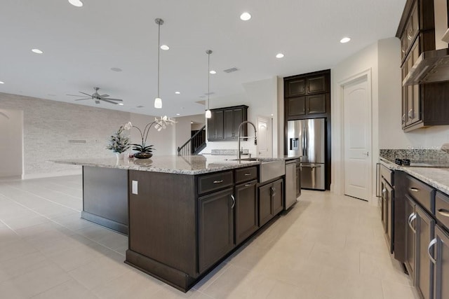 kitchen with pendant lighting, stainless steel appliances, a sink, a large island with sink, and wall chimney exhaust hood