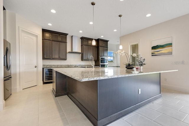 kitchen featuring wall chimney range hood, freestanding refrigerator, a large island with sink, and decorative light fixtures