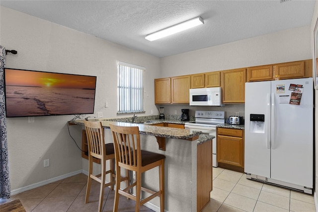 kitchen with kitchen peninsula, a breakfast bar, dark stone countertops, and white appliances