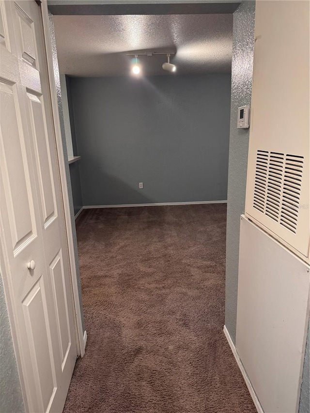 hallway featuring dark carpet, rail lighting, and a textured ceiling