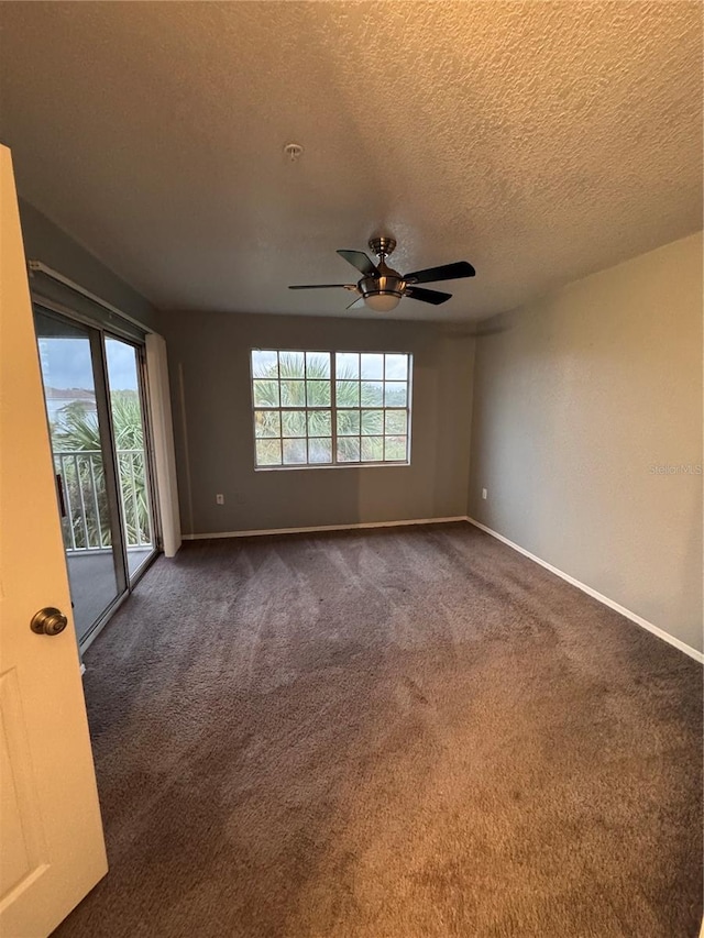 empty room featuring ceiling fan, a textured ceiling, and dark carpet