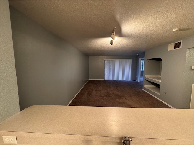 hall featuring dark carpet and a textured ceiling