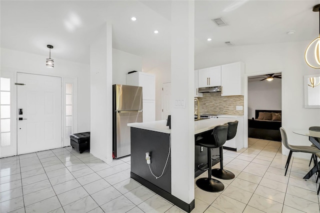 kitchen featuring lofted ceiling, white cabinets, hanging light fixtures, ceiling fan, and stainless steel fridge