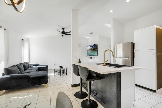 kitchen with a kitchen breakfast bar, ceiling fan, a kitchen island with sink, light tile patterned floors, and stainless steel refrigerator