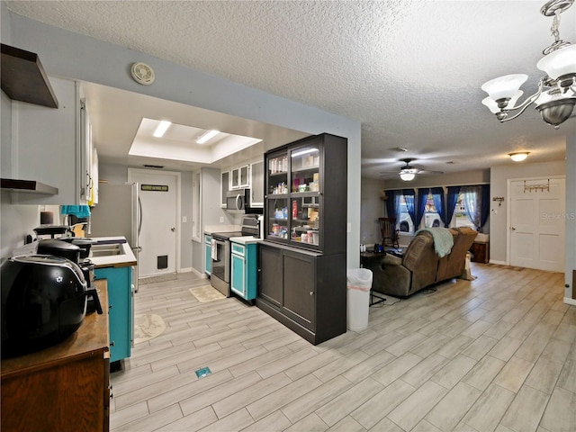 kitchen with a raised ceiling, light wood-type flooring, blue cabinetry, and appliances with stainless steel finishes