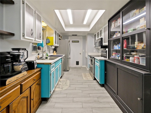 kitchen with a raised ceiling, white cabinetry, blue cabinetry, and appliances with stainless steel finishes