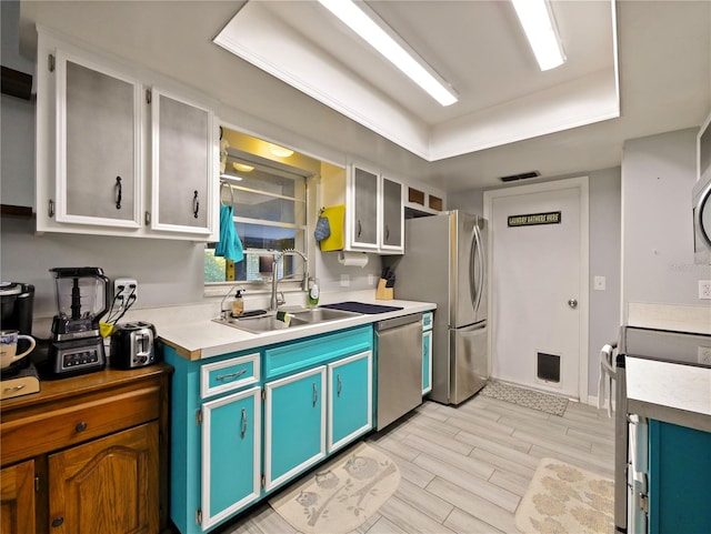 kitchen with white cabinetry, sink, stainless steel appliances, light hardwood / wood-style flooring, and a tray ceiling