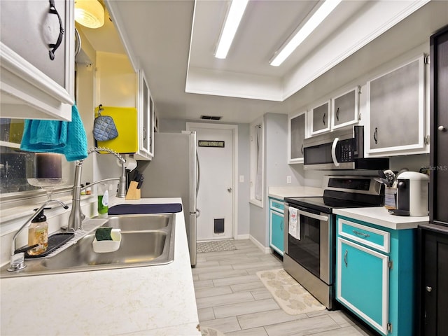 kitchen with stainless steel appliances, a tray ceiling, sink, blue cabinetry, and light hardwood / wood-style floors