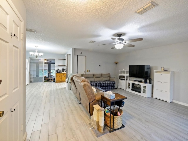 living room with ceiling fan with notable chandelier, light hardwood / wood-style floors, and a textured ceiling