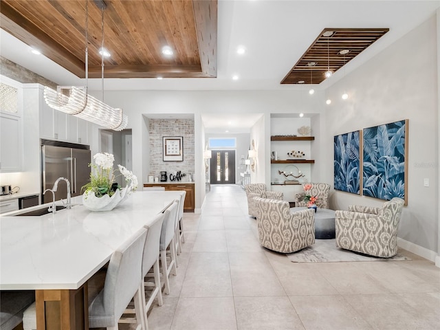 kitchen featuring light stone countertops, stainless steel built in refrigerator, sink, decorative light fixtures, and white cabinetry