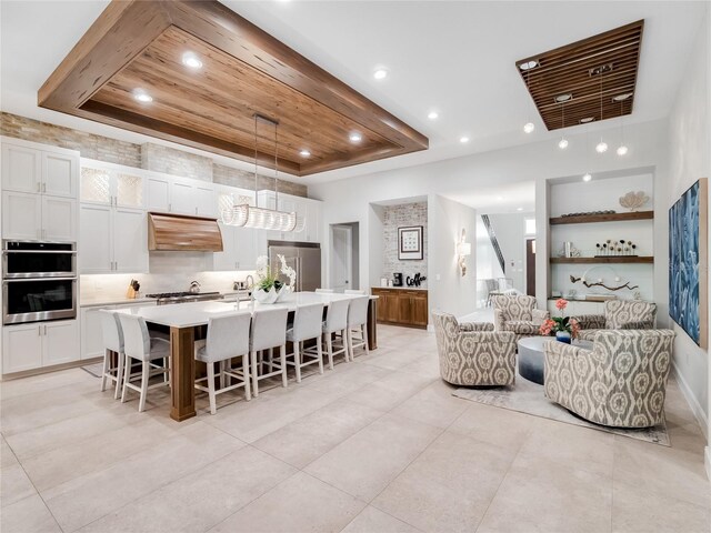 kitchen featuring pendant lighting, a tray ceiling, a kitchen island with sink, a breakfast bar, and white cabinets