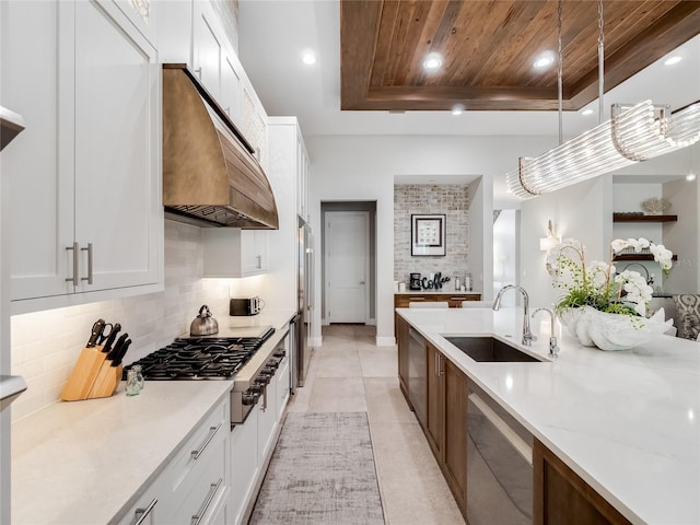 kitchen featuring a tray ceiling, stainless steel appliances, sink, pendant lighting, and white cabinetry