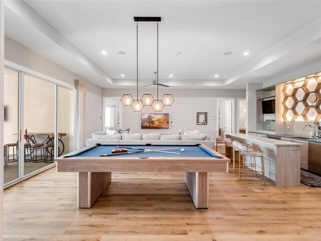 recreation room with a tray ceiling, sink, pool table, and light hardwood / wood-style flooring