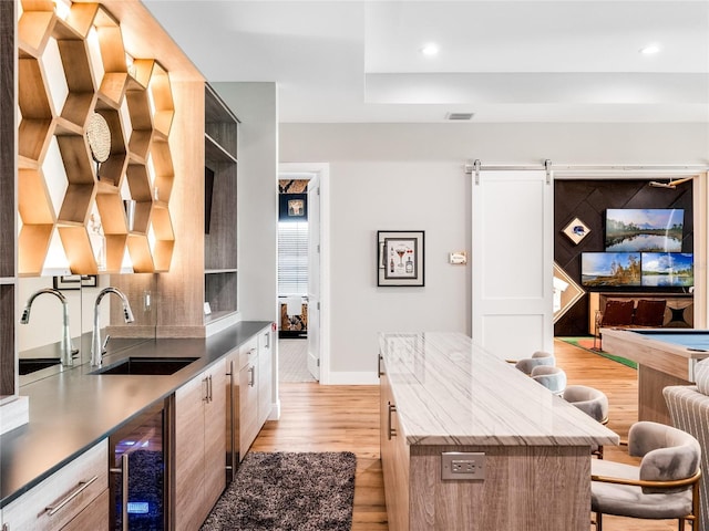 kitchen featuring sink, a barn door, a center island, light hardwood / wood-style floors, and wine cooler