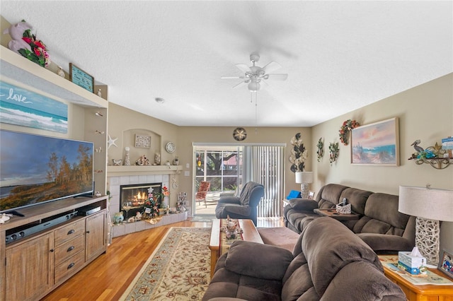 living room featuring hardwood / wood-style floors, ceiling fan, a textured ceiling, and a tiled fireplace