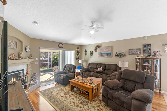 living room with ceiling fan, light wood-type flooring, a textured ceiling, and a tile fireplace