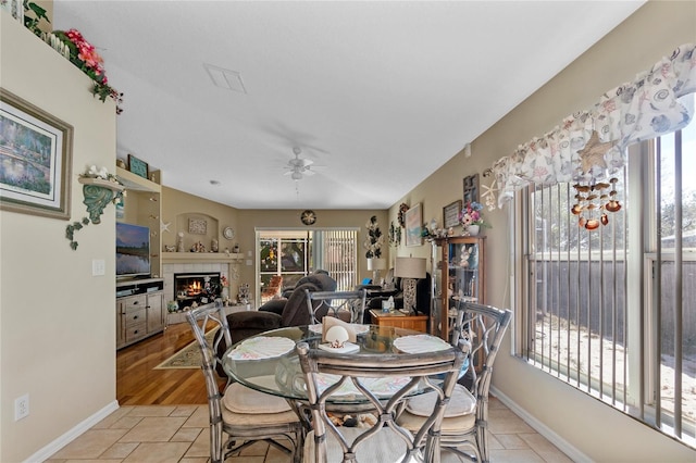 dining area with a tile fireplace, ceiling fan, and light wood-type flooring