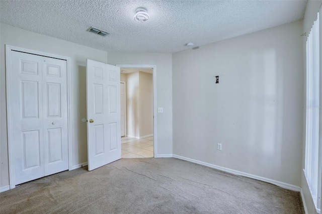 unfurnished bedroom featuring a textured ceiling, light colored carpet, and a closet