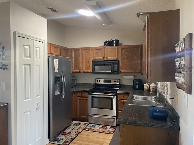 kitchen with a textured ceiling, sink, stainless steel appliances, and light hardwood / wood-style flooring