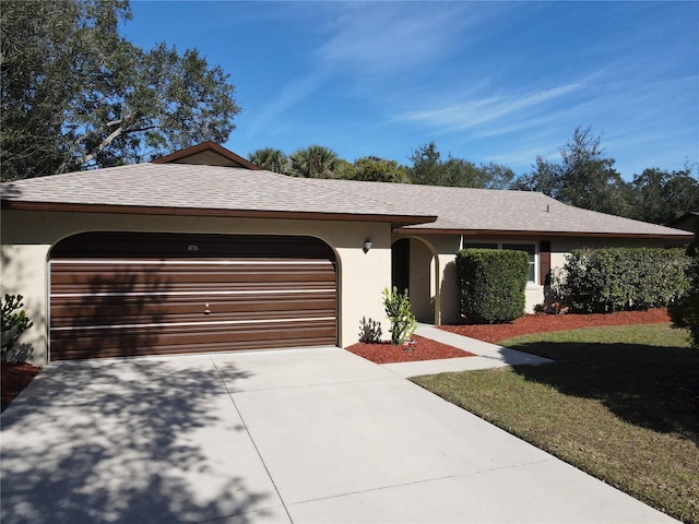 ranch-style house featuring a garage, concrete driveway, roof with shingles, stucco siding, and a front lawn